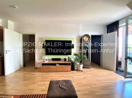 Wohnzimmer mit Parkettboden, Flachbildschirm an dunkler Wand, helle Decke und Glastüren zu Balkon