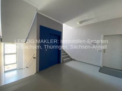 Leerer Gewerberaum mit heller Decke, dunkelblaue Tür, Fenster links, Betonboden