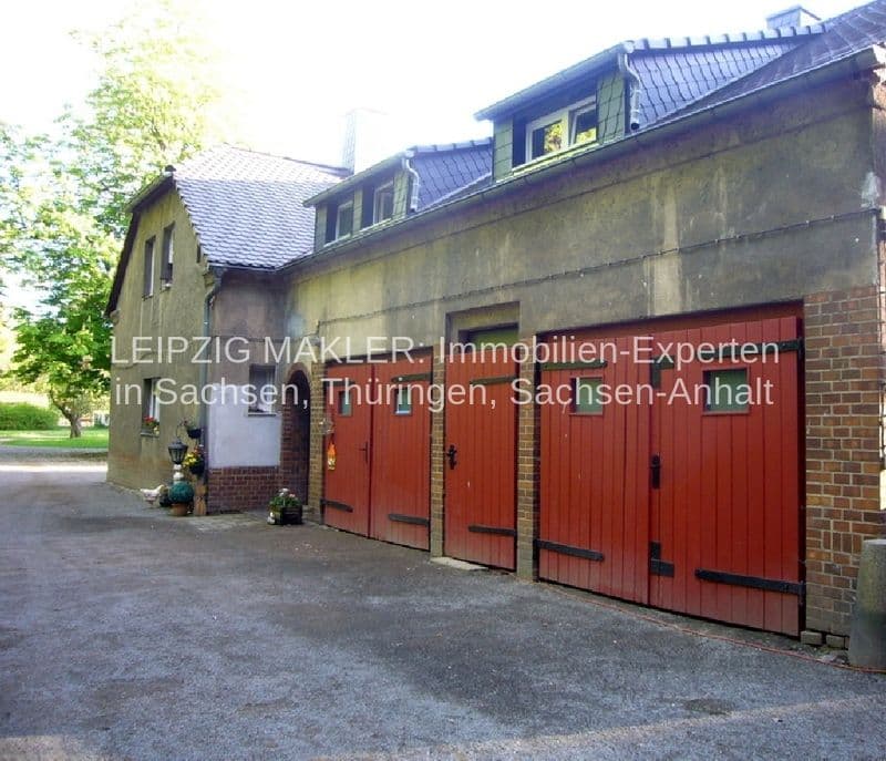 Zweigeschossiges Gebäude mit Satteldach, Ziegelfassade, drei rote Garagentore, Dachgauben, Efeu an der Seite