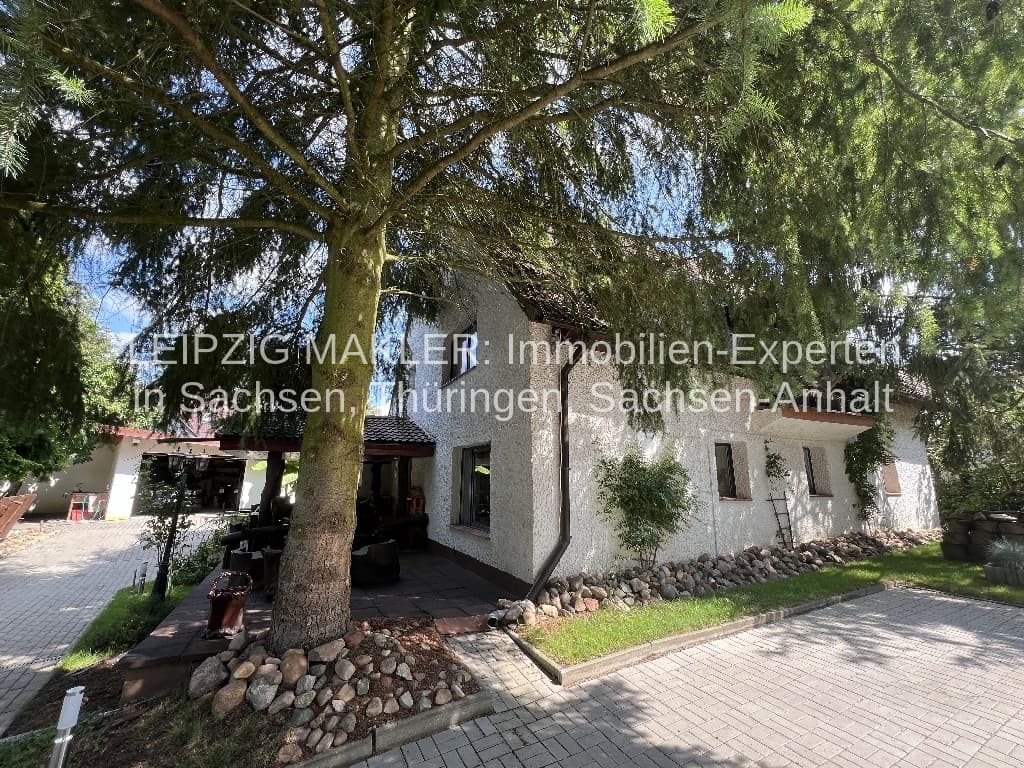 Einstöckiges Wohnhaus mit weißer Fassade, Satteldach und Klinkergiebel, umgeben von großen Bäumen, Splau in Bad Schmiedeberg