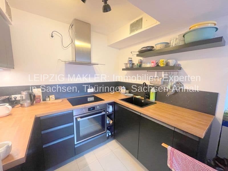 Moderne Küche mit L-förmiger Arbeitsplatte aus Holz, schwarzen Unterschränken, Edelstahl-Kochmulde, Backofen