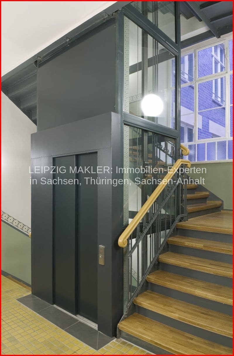 Treppenhaus mit Holzstufen, schwarzer Aufzug, Metallgeländer mit Holzhandlauf, grüne Wandverkleidung unten