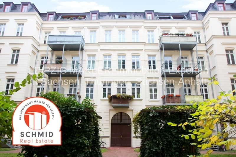 Gründerzeitfassade, vier Geschosse, Mansardendach, moderne Balkone, Eingang mit Rundbogen, grüner Bewuchs
