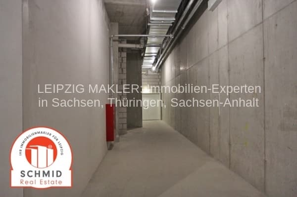 Langer Flur mit Betonwänden, Betonboden und Deckenleuchten, rote Brandschutztür sichtbar