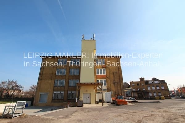 Backsteingebäude mit gelber Fassade und Türmchen, mehrgeschossig, Flachdach mit Antennen, Platz davor, Leipzig-Wahren