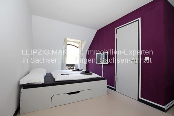 Schlafzimmer mit Einzelbett, Schubladenelement, Kleiderschrank, lila Akzentwand und heller Decke