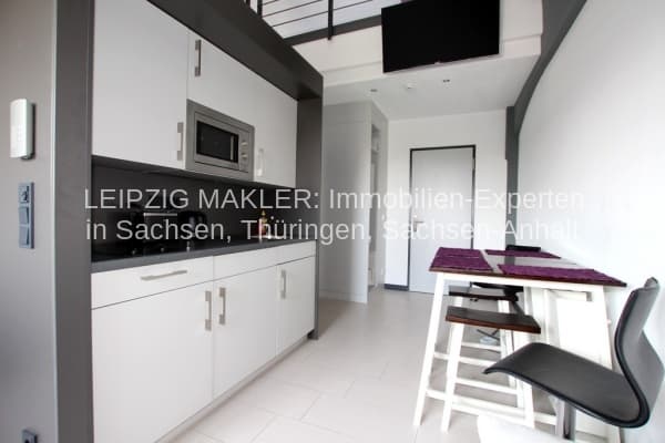 Offene Küche mit weißen Fronten, schwarzer Arbeitsplatte, Essbereich mit Stühlen, Oberlicht