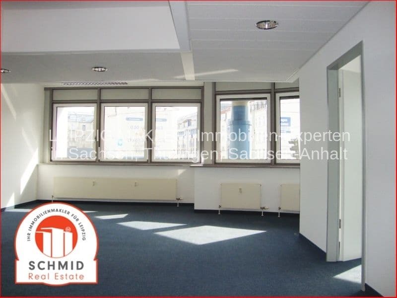 Leerer Büroraum mit Fensterfront, Deckenleuchten, dunklem Bodenbelag, Heizkörpern und Tür zu Nebenraum