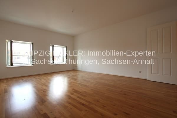 Leeres Wohnzimmer mit Parkettboden, zwei Fenster, weiße Türen, helle Wände