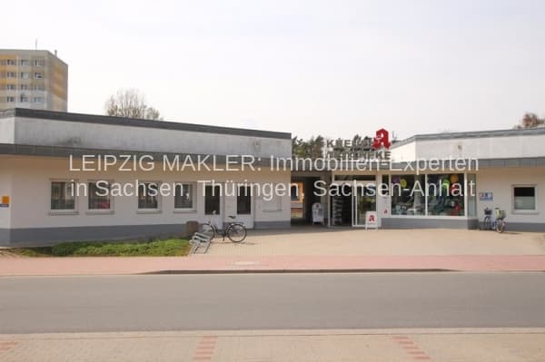 Eingeschossiges Geschäftshaus mit grauer Fassade, flachem Dach und großen Schaufenstern, davor Ziegelpflaster