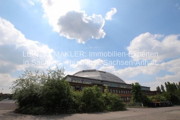 Großes Backsteingebäude mit Kuppeldach, umgeben von Grün, unter blauem Himmel mit Wolken