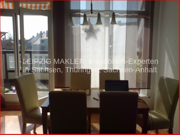 Wohnzimmer mit Esstisch, vier Stühlen, großem Fenster mit Balkonblick und hellen Gardinen