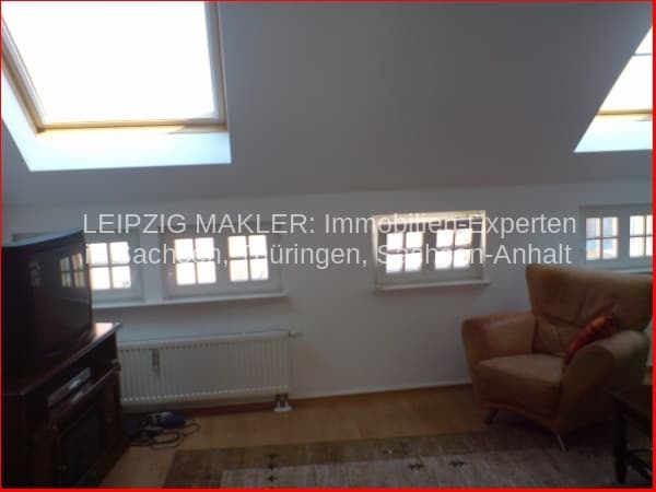 Dachgeschossraum mit zwei Dachflächenfenstern, weißen Wänden, Parkettboden, Heizkörper und braunem Sessel