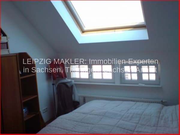 Dachgeschosszimmer mit Dachfenster, Einzelbett, Holzregal und Heizkörper
