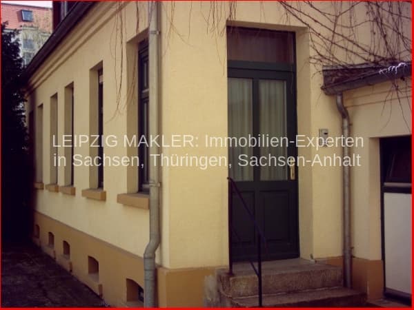 Einstöckiges Haus mit cremefarbener Fassade, dunklen Holzfenstern und Sockelzone in Sandsteinoptik, Efeu an der Ecke