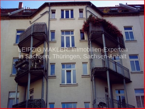 Vier-Geschoss-Wohnhaus mit Putzfassade, Fensterfluchten, seitlichen Balkonen mit Metallgeländern und Efeu-Bewuchs