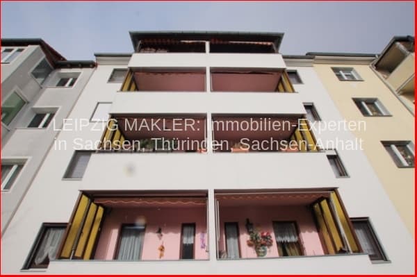 Viergeschossiges Wohnhaus mit weißer Putzfassade, roten Balkonen und gelben Fensterrahmen