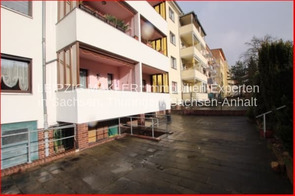 Mehrfamilienhaus mit drei Geschossen, Flachdach, weiße Putzfassade, Balkon im Erdgeschoss, Ziegelsockel