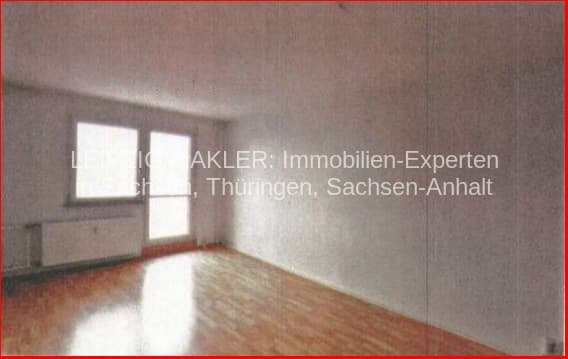 Leerer Wohnraum mit Parkettboden, zwei Fenster mit Jalousien, helle Wände, Heizkörper