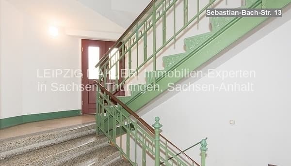 Treppenhaus mit grünem Geländer und roter Eingangstür, Fliesenboden, weiße Wände
