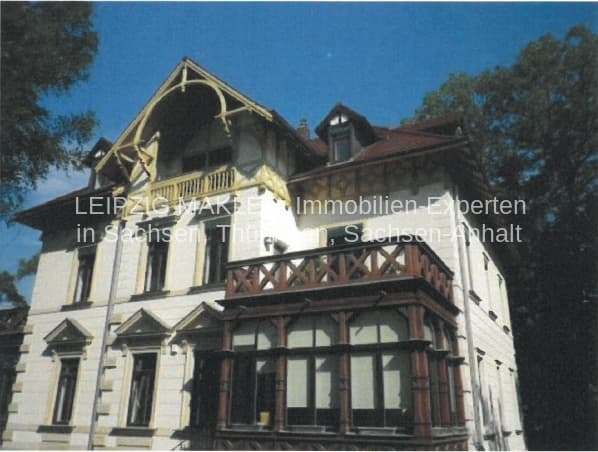 Dreigeschossige Villa mit Mansarddach und Balkon, verputzte Fassade mit roten Dachziegeln, Bäume ringsum