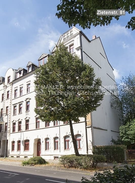 Viergeschossiges Wohnhaus mit Mansarddach, heller Fassade und roten Fensterrahmungen, Efeu an der Seite