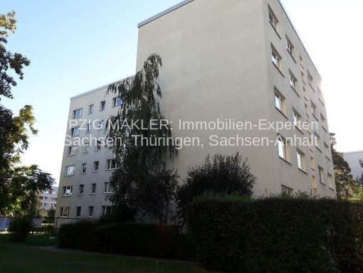 Vierstöckiges Wohngebäude mit heller Fassade und regelmäßiger Fensteranordnung, umgeben von Grünfläche und Hecken