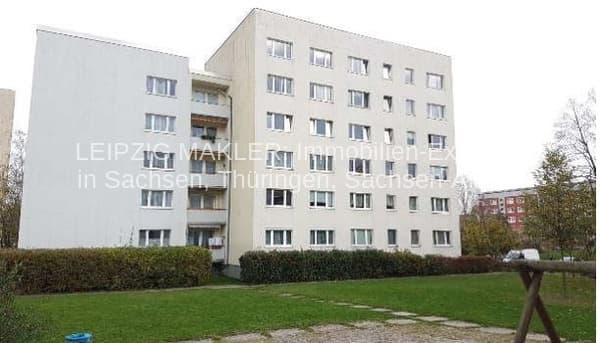 Fünfgeschossiger Wohnblock mit verputzter Fassade, regelmäßigen Fensterreihen und Balkonen, Grünfläche davor