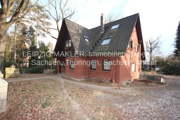 Zweigeschossiges Einfamilienhaus mit Satteldach, Ziegelfassade und Dachgauben, umgeben von Bäumen und Kiesauffahrt