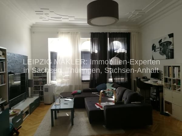Wohnzimmer mit schwarzem Ecksofa, Parkett, weißer Decke mit schwarzer Pendelleuchte, Fenster mit Gardinen, Regale