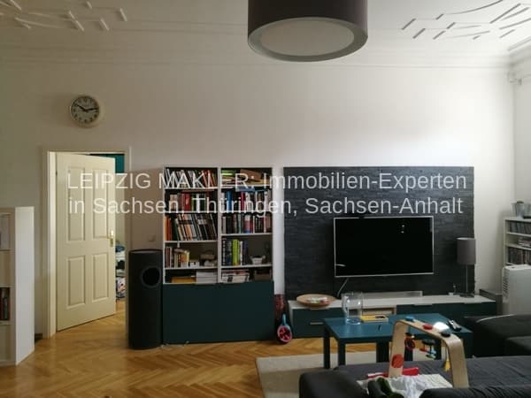Wohnzimmer mit Parketboden, weißer Decke, eingebauter Schrankwand mit Regalen und schwarzem TV-Möbel