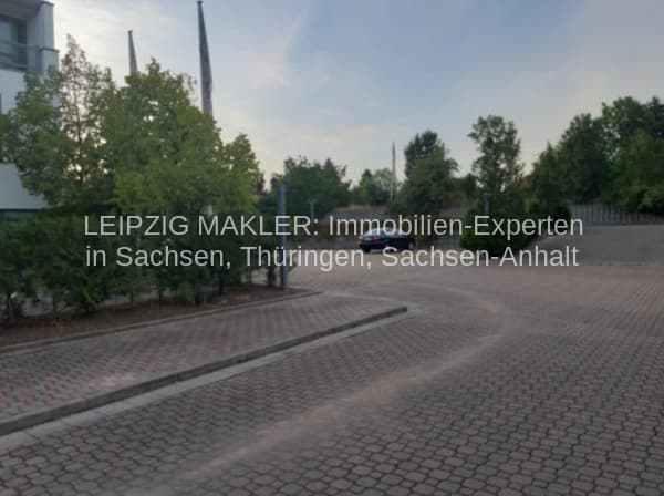 Gepflasterter Platz mit Grünstreifen und Bäumen, Gebäude im Hintergrund, Hallesche Straße in Leipzig