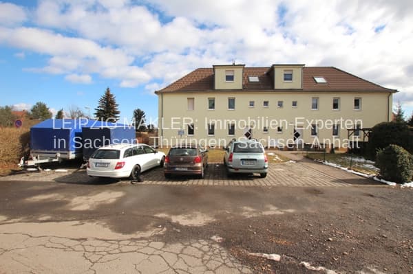 Mehrfamilienhaus mit Mansardendach, beige Fassade, braune Dachziegel, Parkplatz mit Autos, Steigerweg in Deutzen