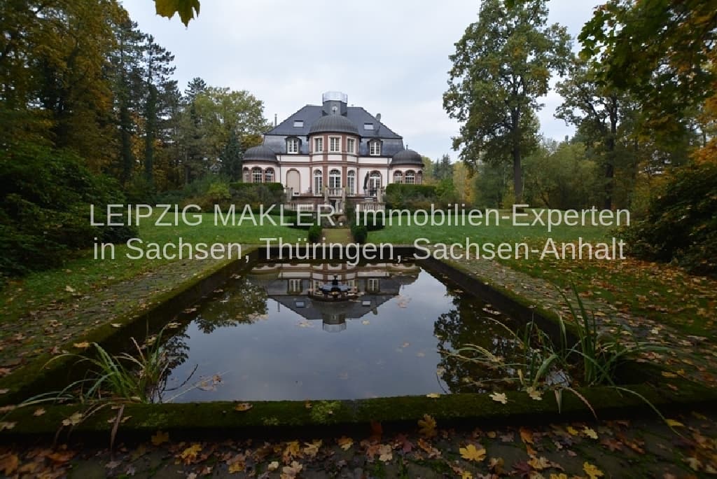 Villa mit Mansarddach und Putzfassade spiegelt sich in Teich, umgeben von Laubbäumen, Waldweg in Beucha
