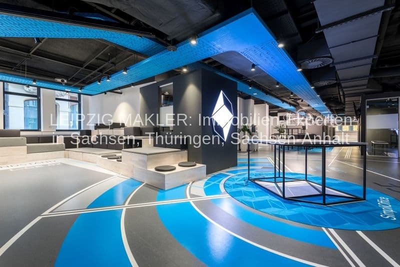 Modernes Bürogebäude mit offener Grundfläche, Betonboden in Blau und Grau mit geometrischen Mustern, blaue Deckenelemente