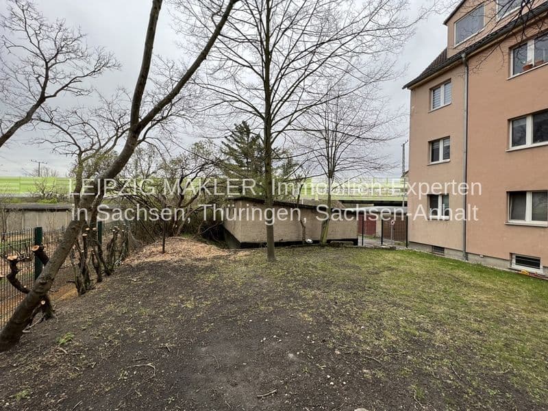 Garten mit Kiesflaeche und Rasen, kahle Baeume, rechts dreigeschossiges Wohnhaus mit beiger Fassade