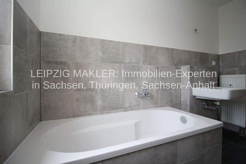 Badezimmer mit weißer Badewanne, grauen Feinsteinzeugfliesen an den Wänden, weißem Waschbecken und Heizkörper