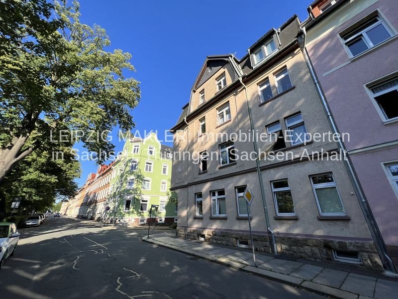 Gründerzeitgebäude mit Mansardendach und Schieferfassade, daneben grünes Wohnhaus, Straßenansicht mit Bäumen