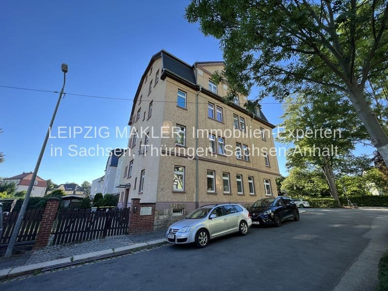 Vier-Geschoss-Wohnhaus mit Satteldach, Ziegelfassade, regelmäßigen Fensterreihen, Ziegelsockel, umgeben von Bäumen