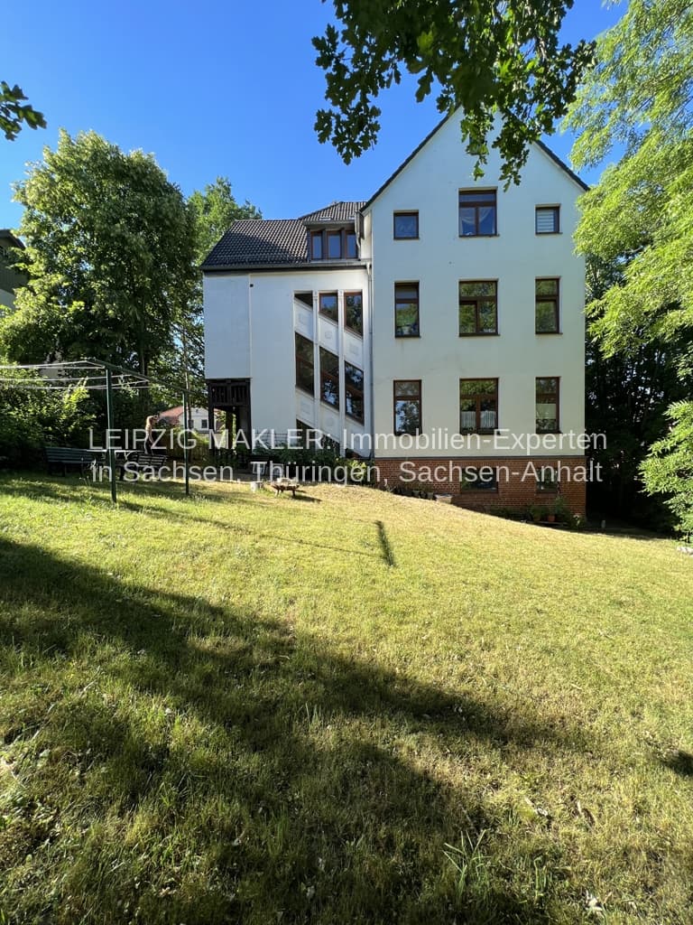 Mehrfamilienhaus mit drei Geschossen, weißer Fassade und dunklem Satteldach, große Fenster, Balkon