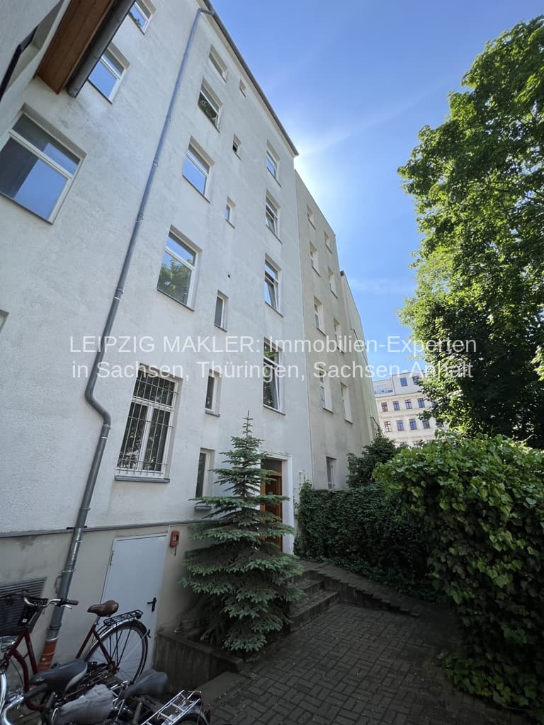 Fünfgeschossiges Wohngebäude mit weißer Putzfassade, regelmäßig angeordneten Fensterreihen und Efeu an der Seite