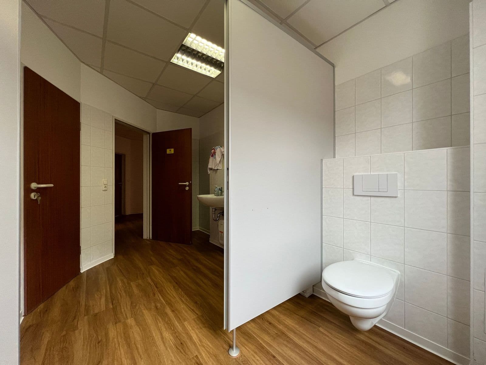 Sanitärraum mit Toilette, weiße Wandfliesen, Holzparkett, offene Tür zu Flur mit weiteren Türen