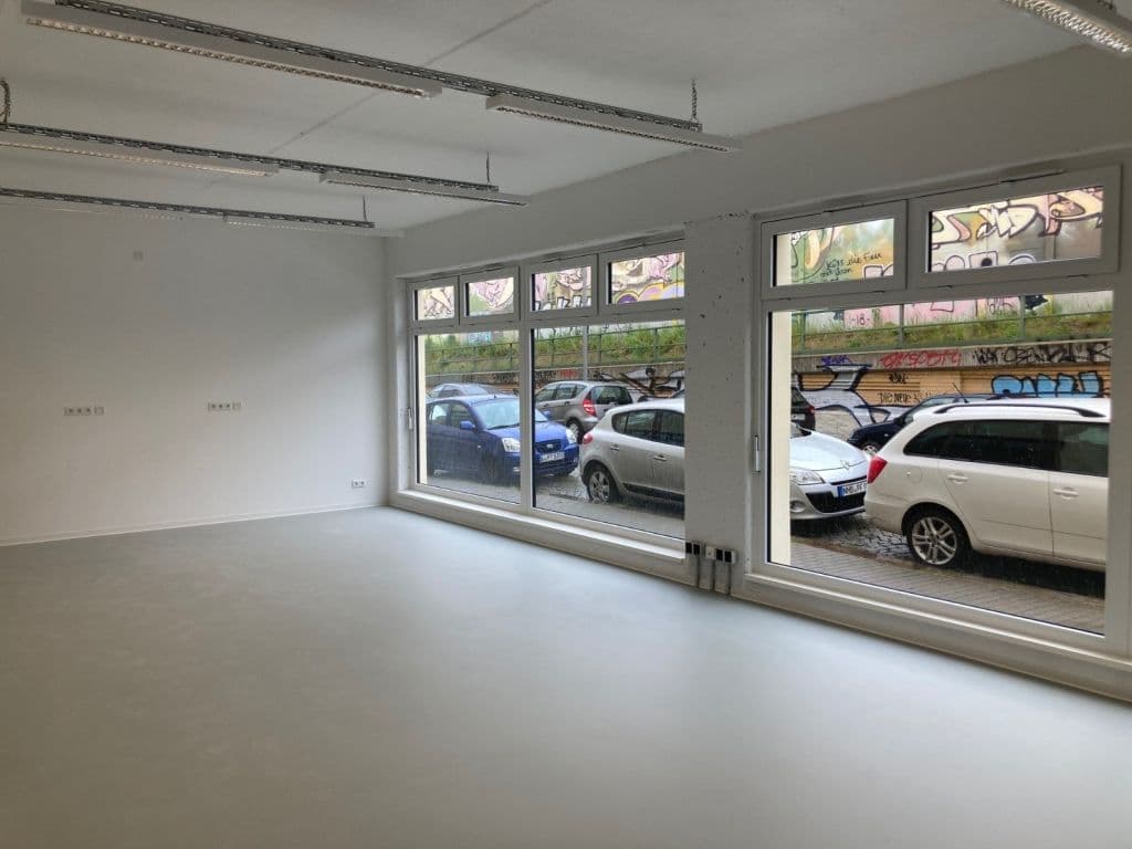 Leerer Laden mit großflächiger Fensterfront zu Parkplatz, Betondecke mit Installationsschienen, weiße Wände