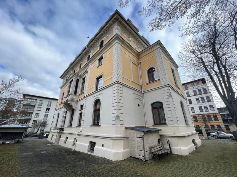 Gründerzeitbau mit Walmdach, gelber Putzfassade im Obergeschoss, weiße Sockeletage, Rustikaquaderung, rundbogige Fenster