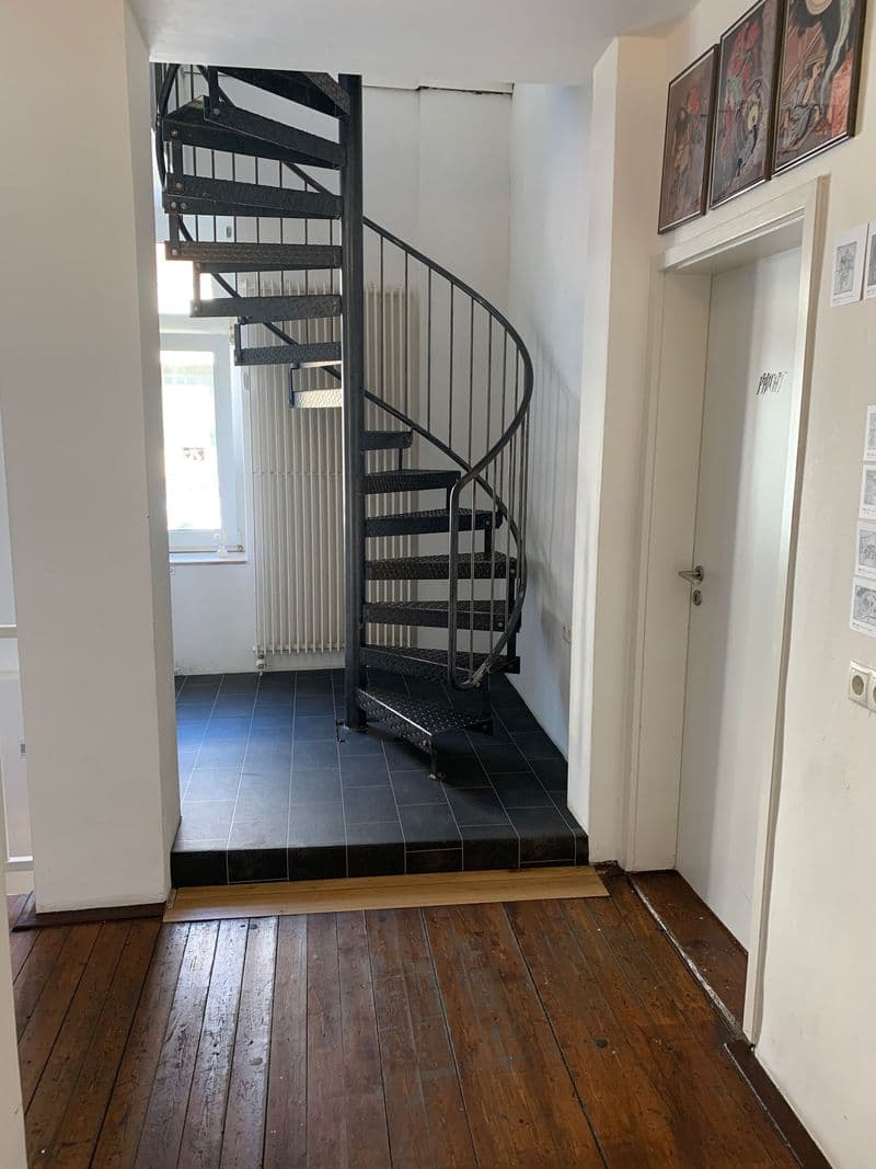 Flur mit Holzparkett und schwarze Wendeltreppe aus Metall, weißgetünchte Wände, Tür rechts