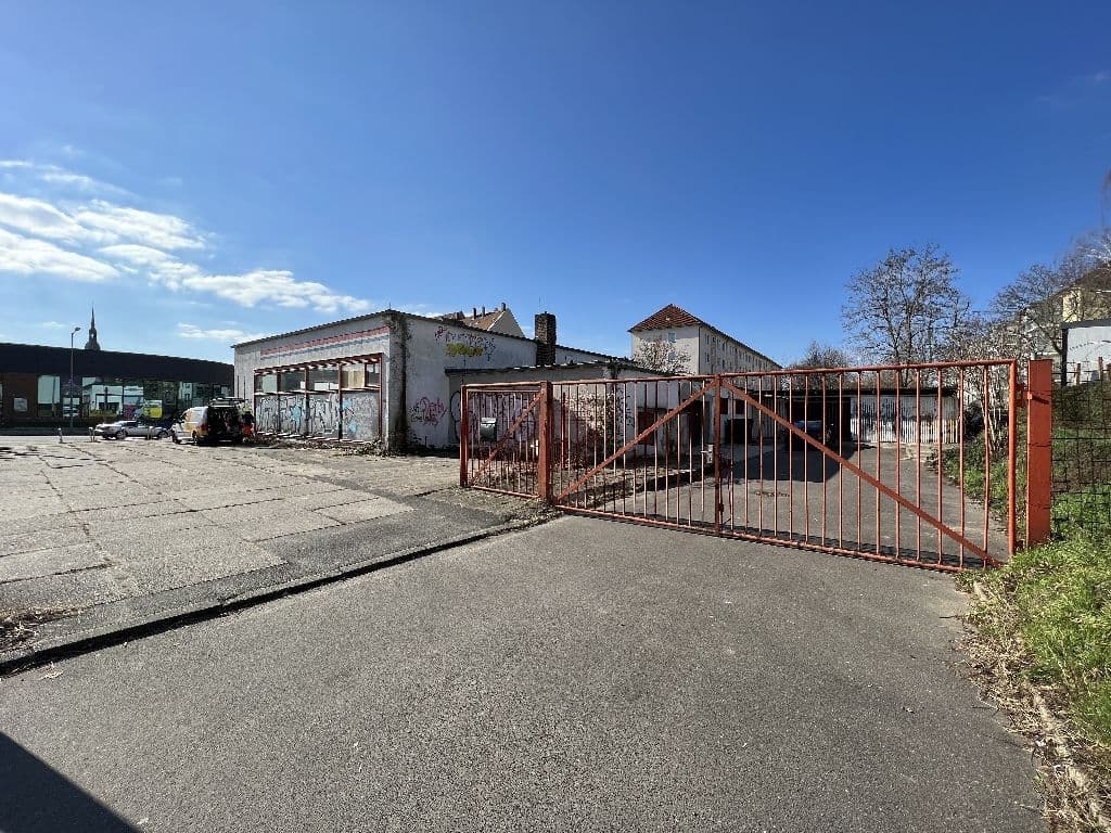 Gewerbefläche mit verfallenen einstöckigen Gebäuden, rostigem Metalltor und Betonplatz, Leonhard-Frank-Straße in Leipzig
