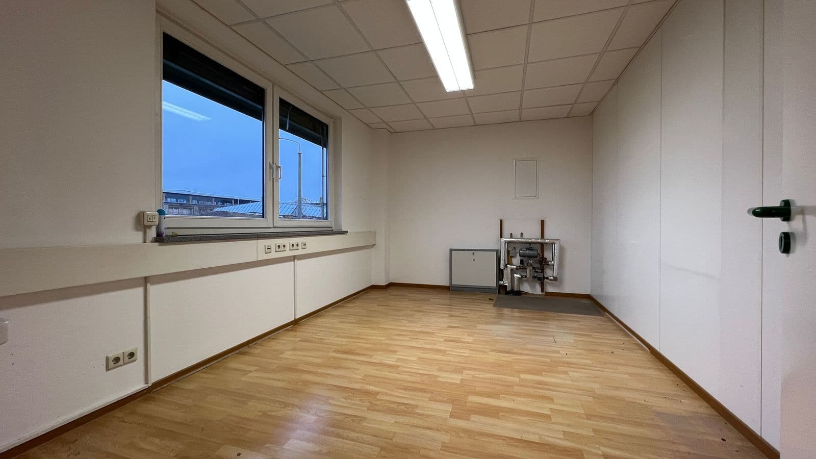 Leerer Büroraum mit Holzparkett, weiße Wände, lange Arbeitsfläche unter Fenster, Deckenleuchte