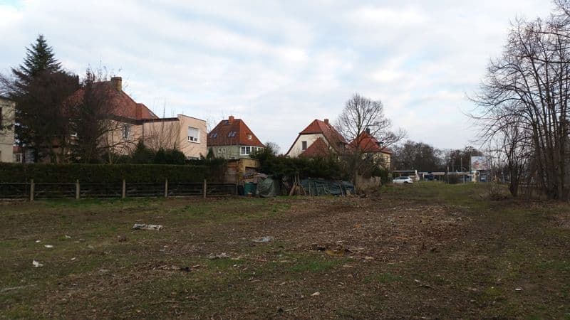 Grundstück mit Holzzaun, dahinter Wohnhäuser mit Ziegeldächern und Gärten, Prager Straße in Leipzig