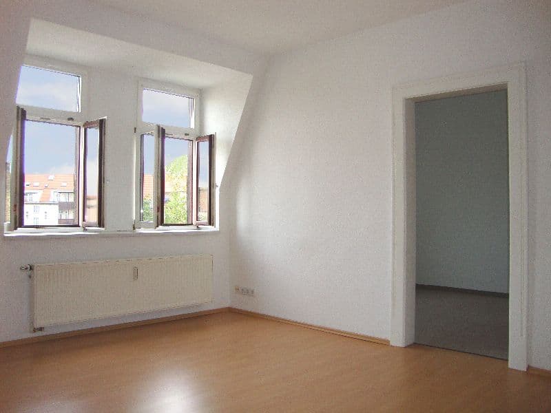 Leeres Zimmer mit Dachschräge, zwei geöffnete Fenster mit Holzrahmen, Heizkörper, Laminatboden, offene Tür zu Nebenraum