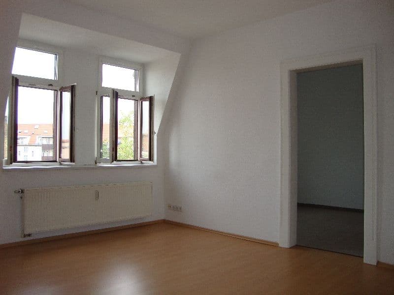 Leeres Zimmer mit Parkettboden, zwei Fenster mit Holzrahmen, Heizkörper, offene Tür zu Nebenraum